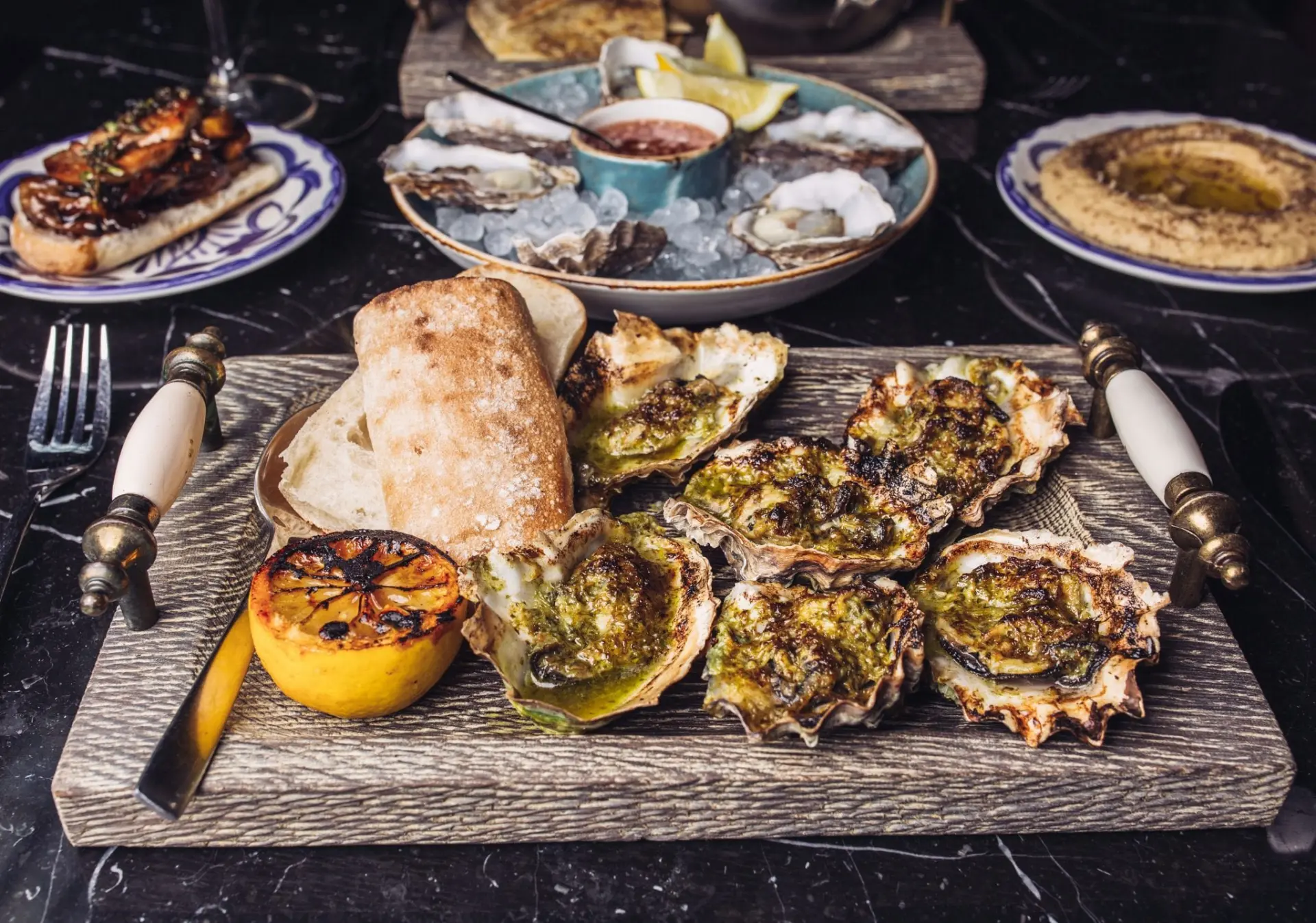 various plates on table with grilled and raw oysters and hummus