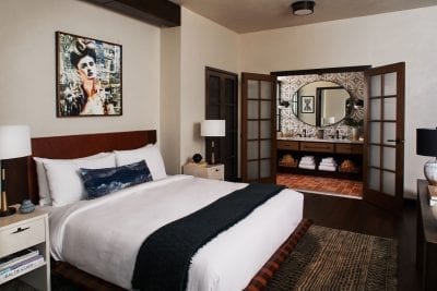 hotel bedroom with nightstands, and bathroom with mirror and towels underneath