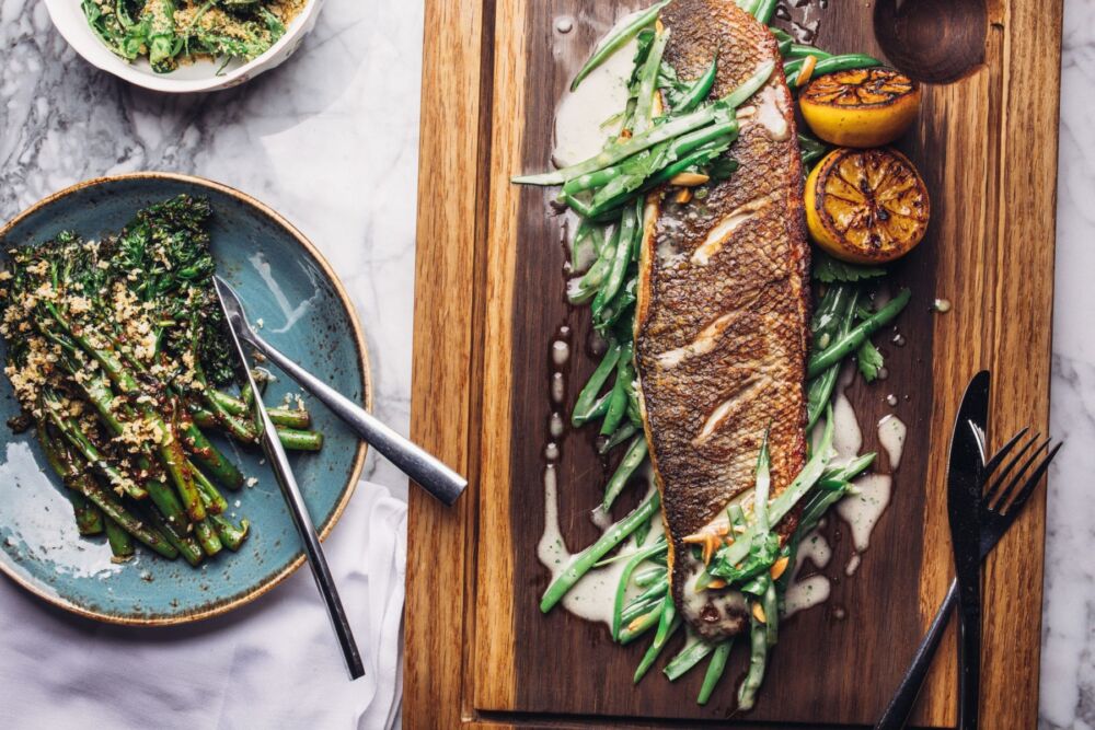 grilled european sea bass on wooden board and topped with peas
