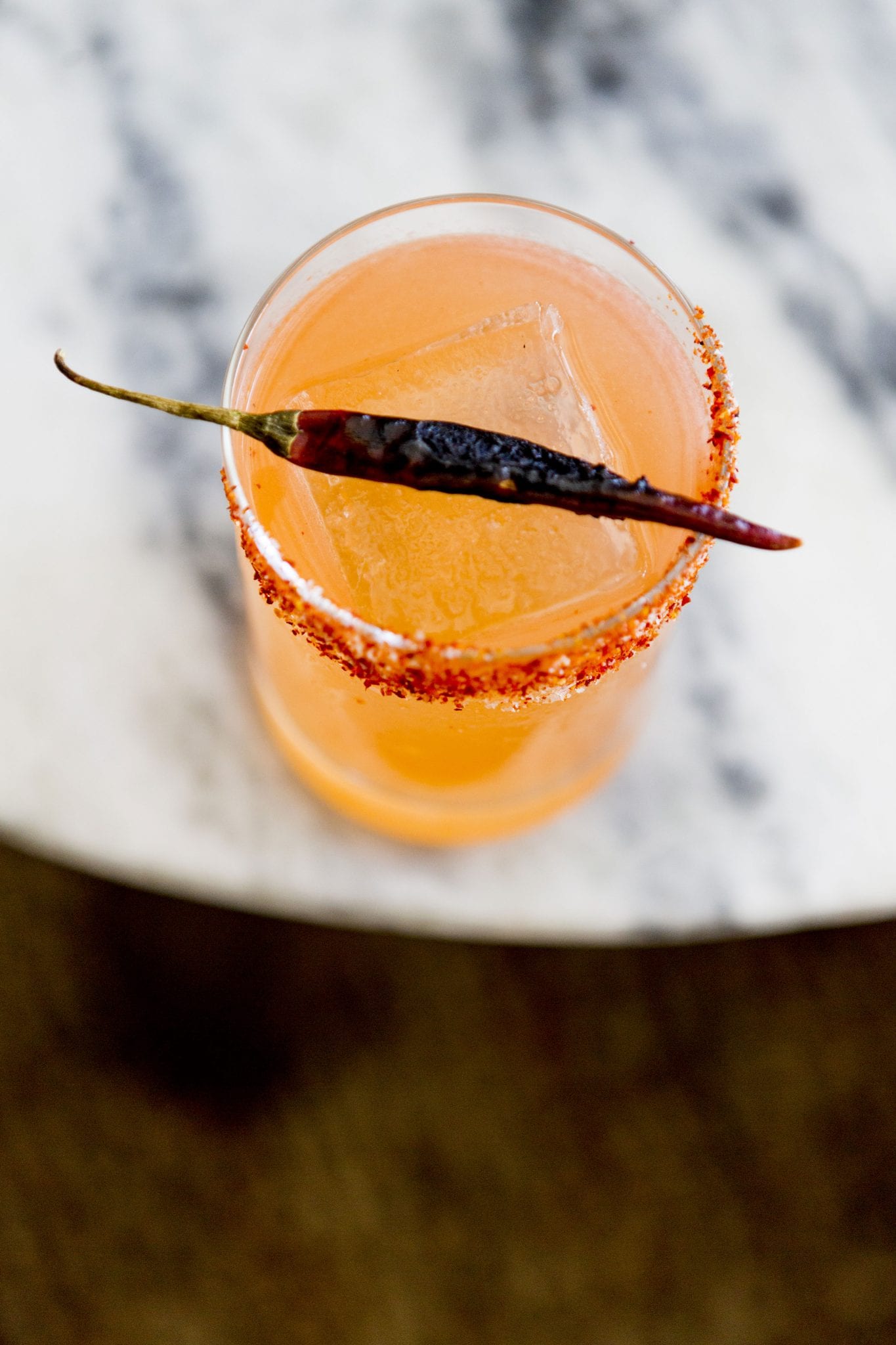 overhead view of cocktail with chilli on rim and grilled chilli pepper resting on rim of glass