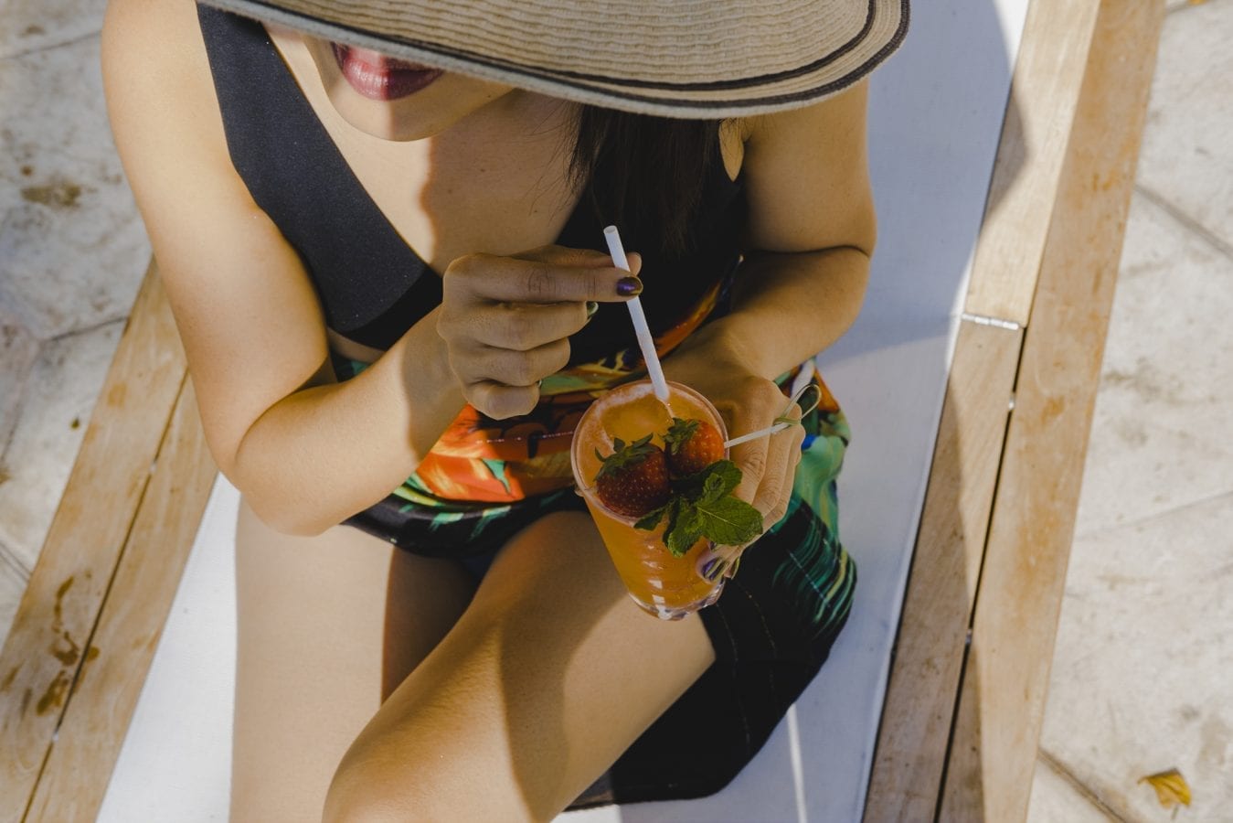 overhead view of woman wearing a hat and sipping a cocktail