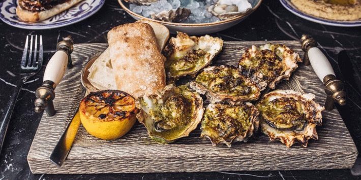 cutting wood board with grilled oysters, lime and toasted bread