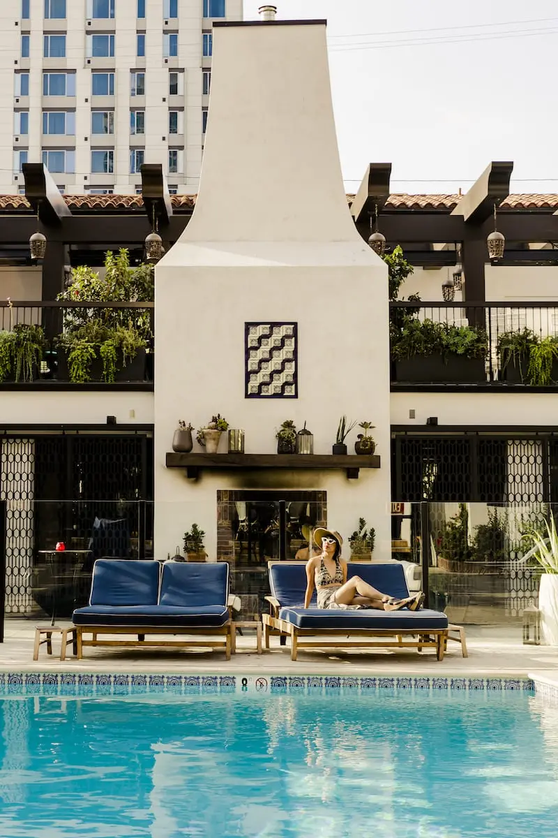 woman sitting on wide lounge chair in front of fireplace, next to outdoor pool